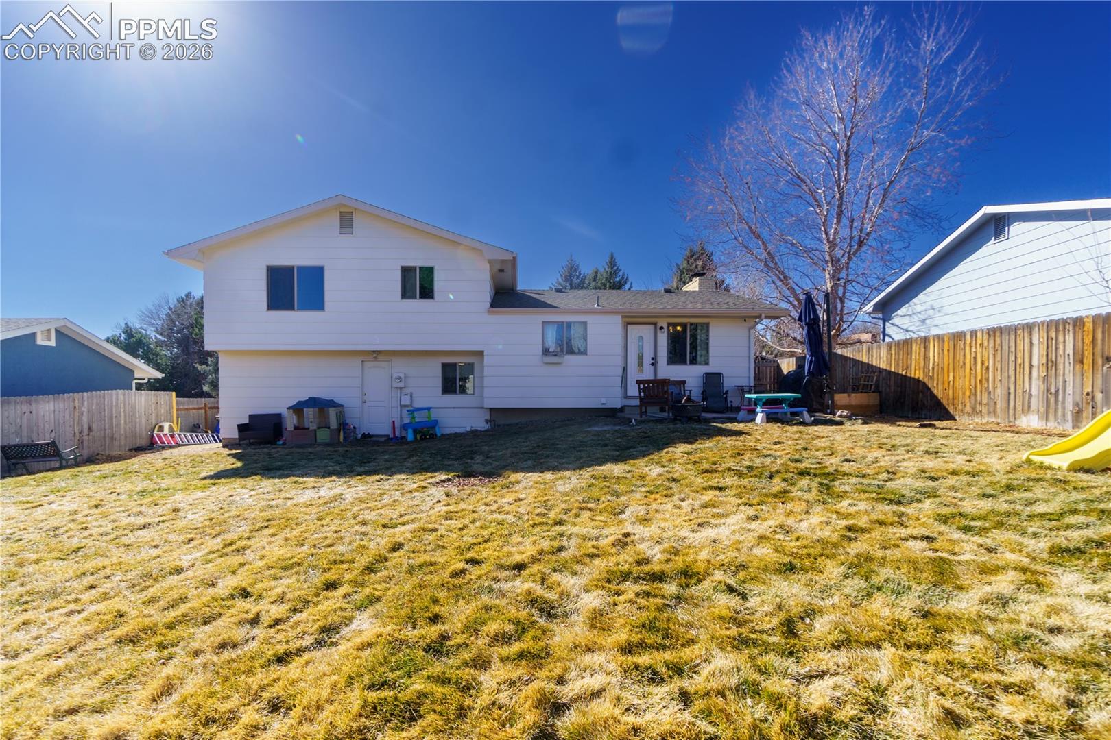 Back of property with entry steps, a fenced backyard, a chimney, and a lawn