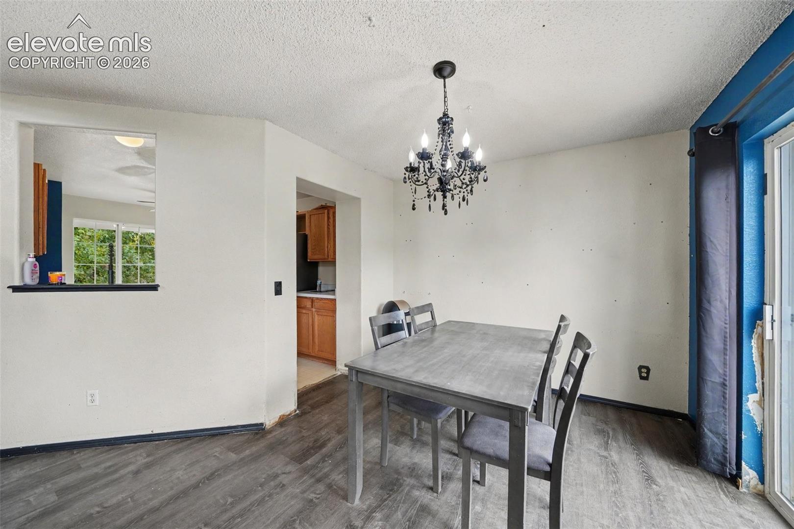 Dining area featuring wood-finish flooring, a decorative multi-arm chandelier, and a pass-through window looking toward the kitchen