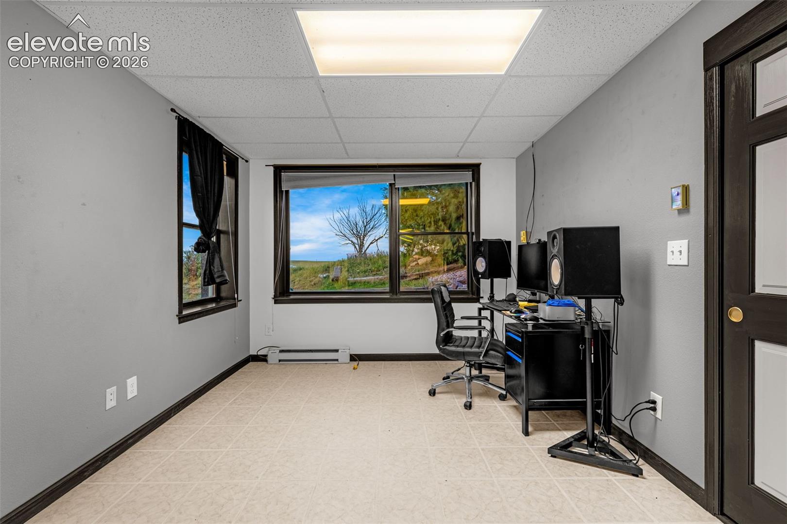 Drop ceiling with integrated fluorescent lighting, neutral-toned flooring, and multiple windows providing natural illumination