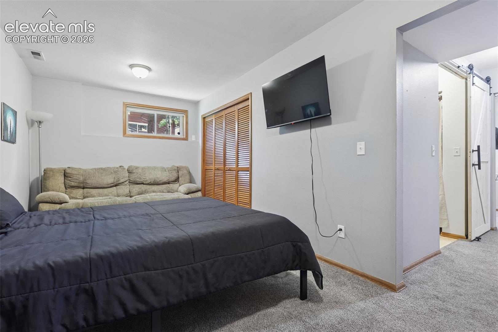 Carpeted flooring with light gray walls, a built-in closet with louvered bifold doors, and a window with wood trim