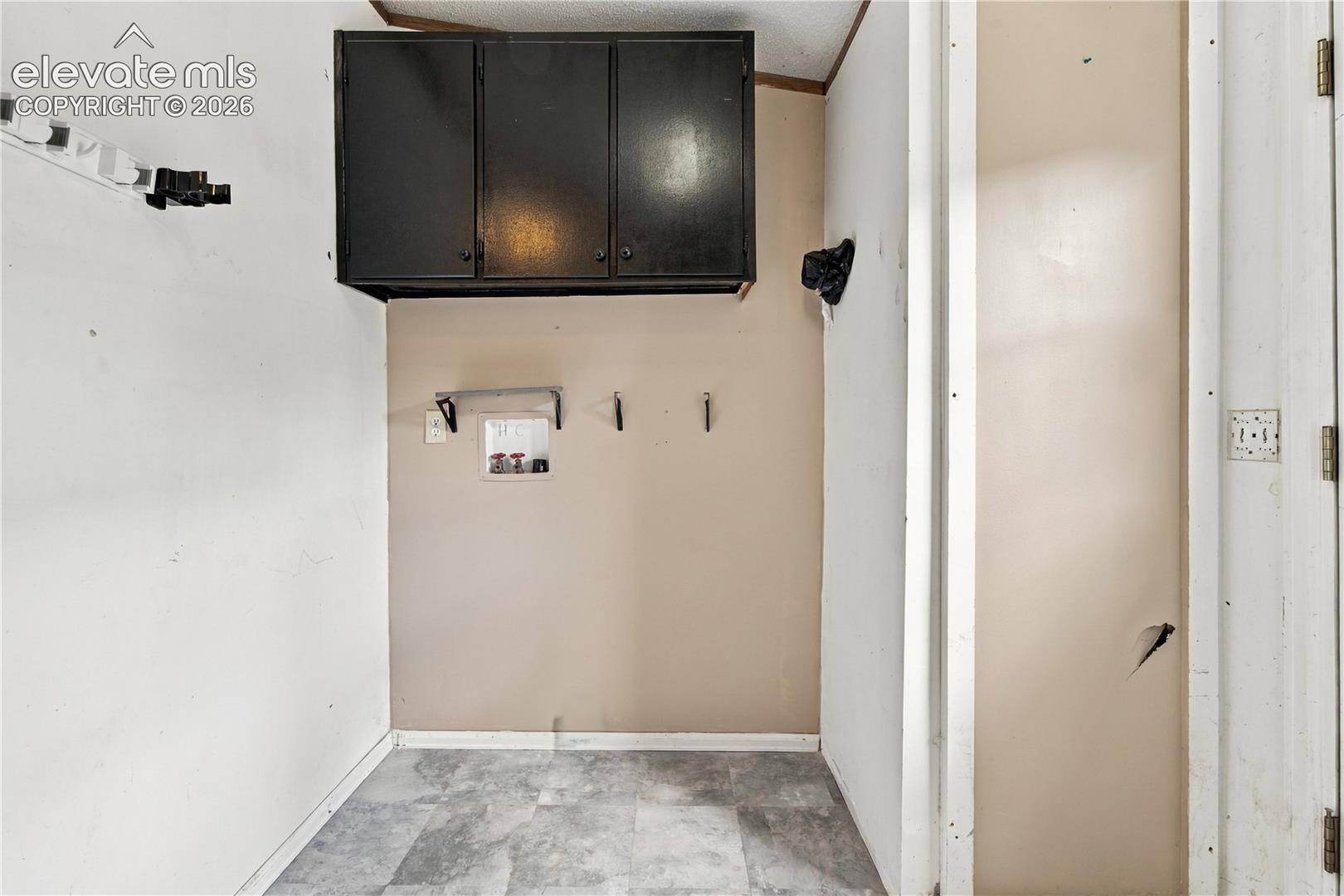 Utility area featuring overhead cabinetry, wall-mounted storage, and a durable flooring surface