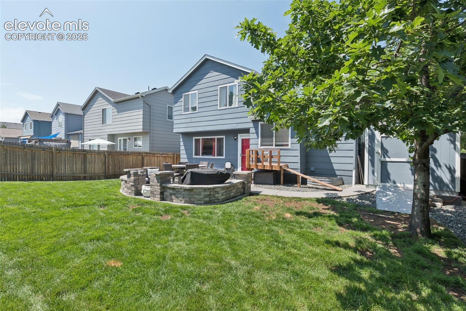 Expansive backyard featuring a stone-clad fire pit, concrete patio, privacy fencing, and mature trees