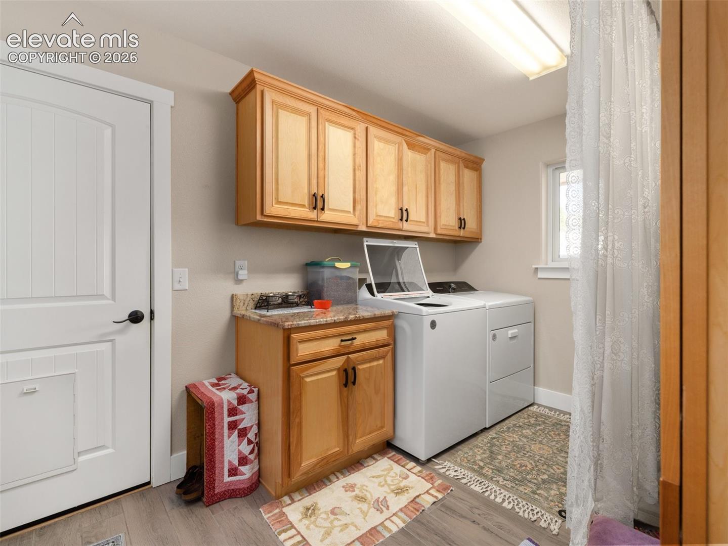 Laundry area with wood-finish cabinetry, light wood-finish flooring, and a window