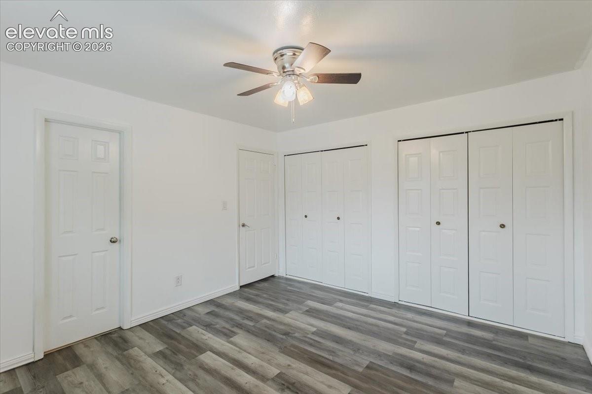 Spacious room featuring wood-finish flooring, bright white walls, two sets of bifold closet doors, and a ceiling fan with integrated lighting