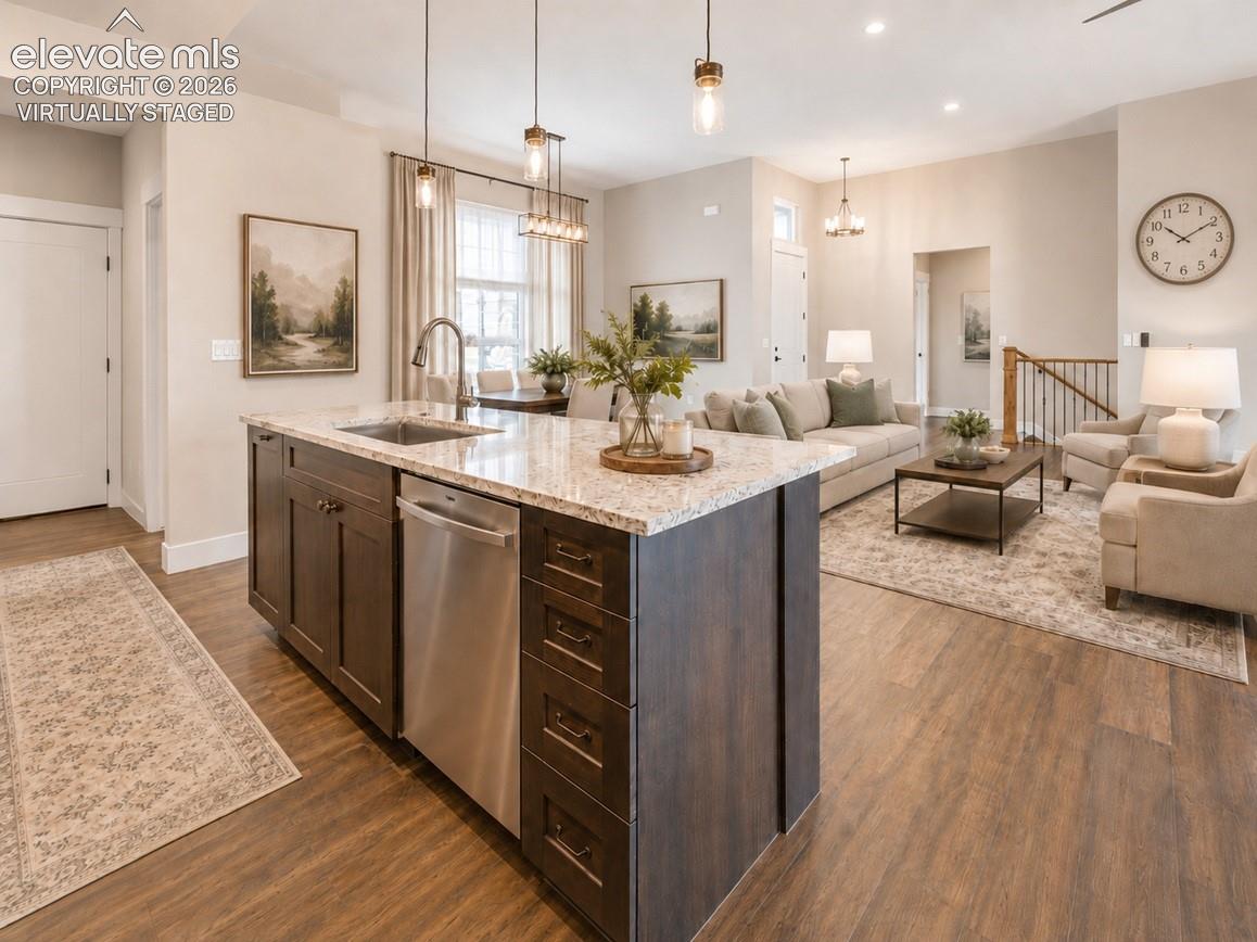 Virtually Staged Open-concept living space featuring wood-finish flooring, a kitchen island with stone-finish countertops, stainless steel appliances, recessed lighting, and a staircase with wood newel posts and railings