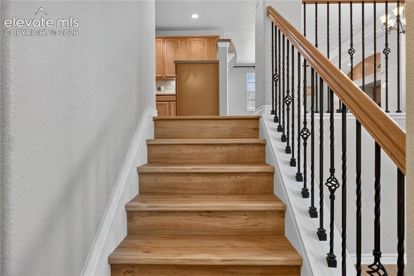 Staircase featuring brand new LVP treads, a wooden handrail, and wrought-iron balusters with decorative scrollwork