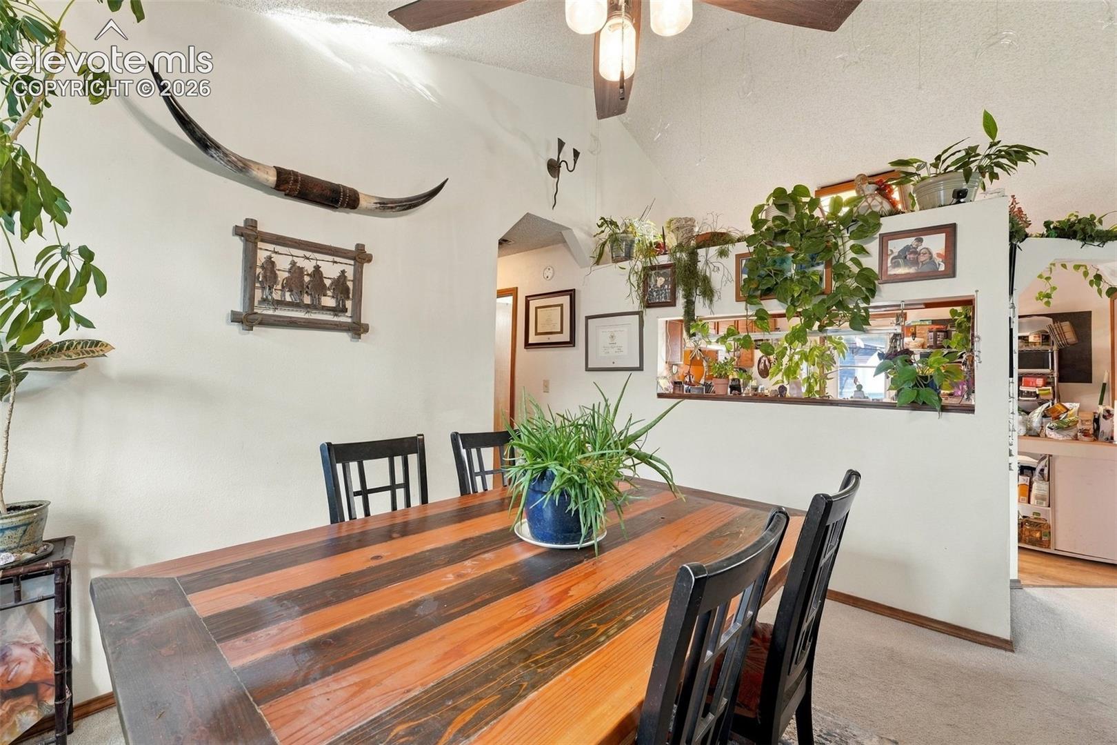 Vaulted ceiling featuring a ceiling fan with integrated lighting and a pass-through wall cutout