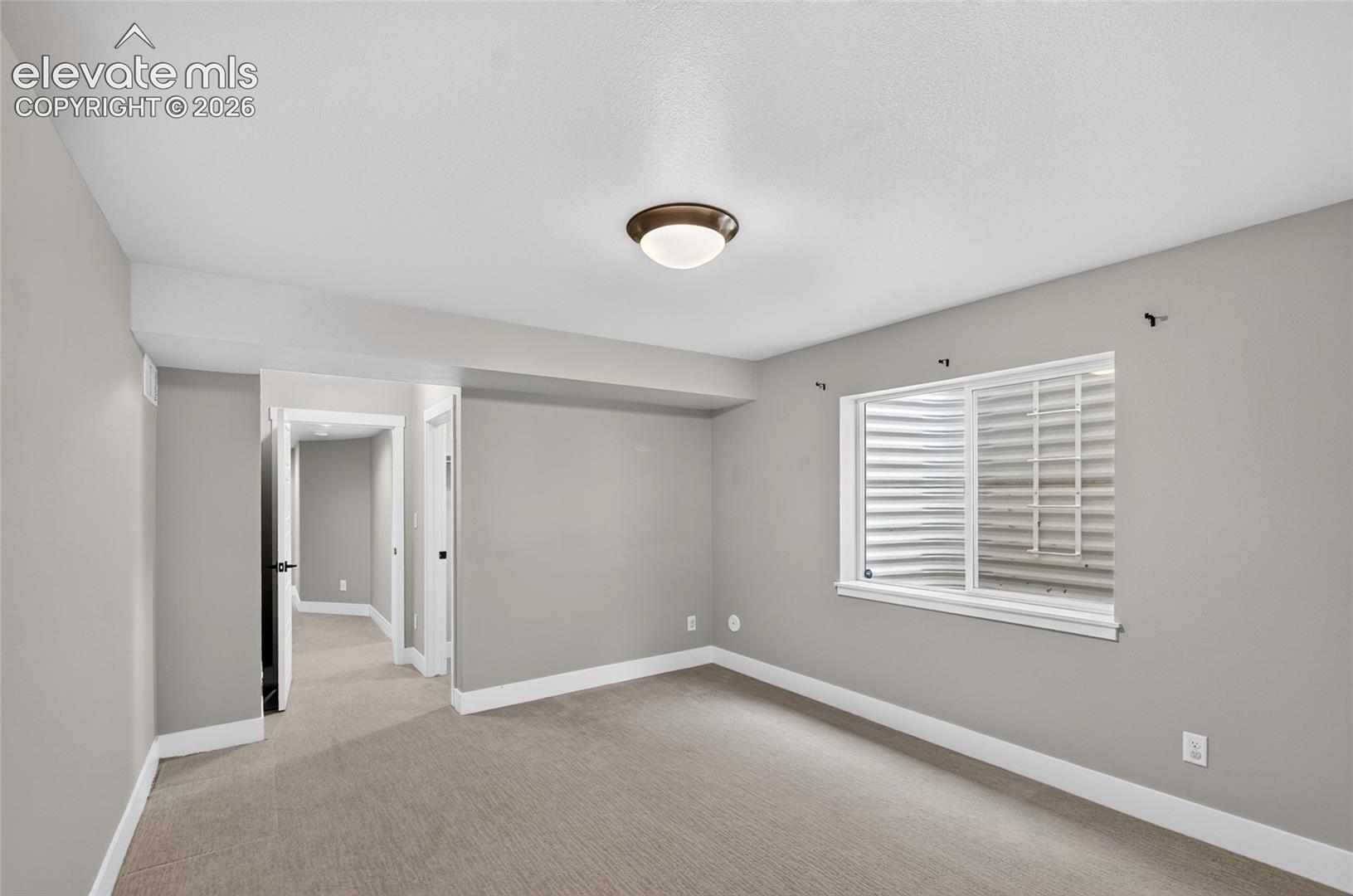 Neutral tone walls with white baseboards, a flush-mount ceiling light, and carpeted flooring-with hallway between 2 lower level bedrooms