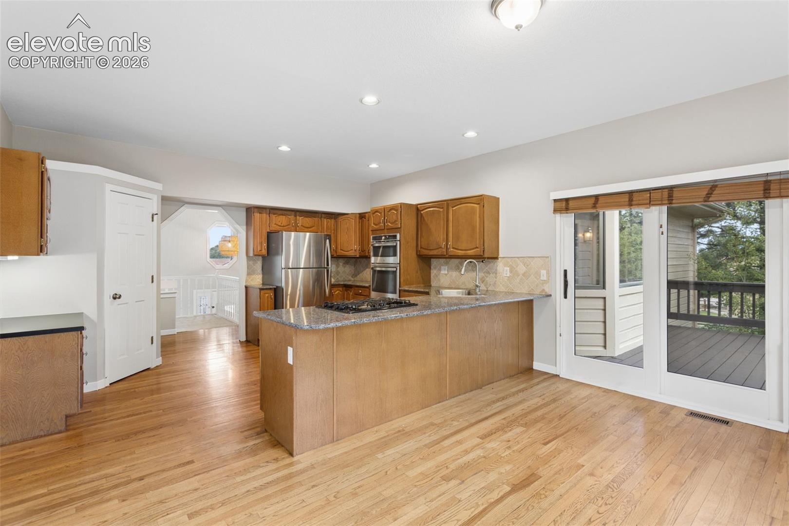 Open kitchen with wood-finish flooring, recessed lighting, and a kitchen island with cooktop