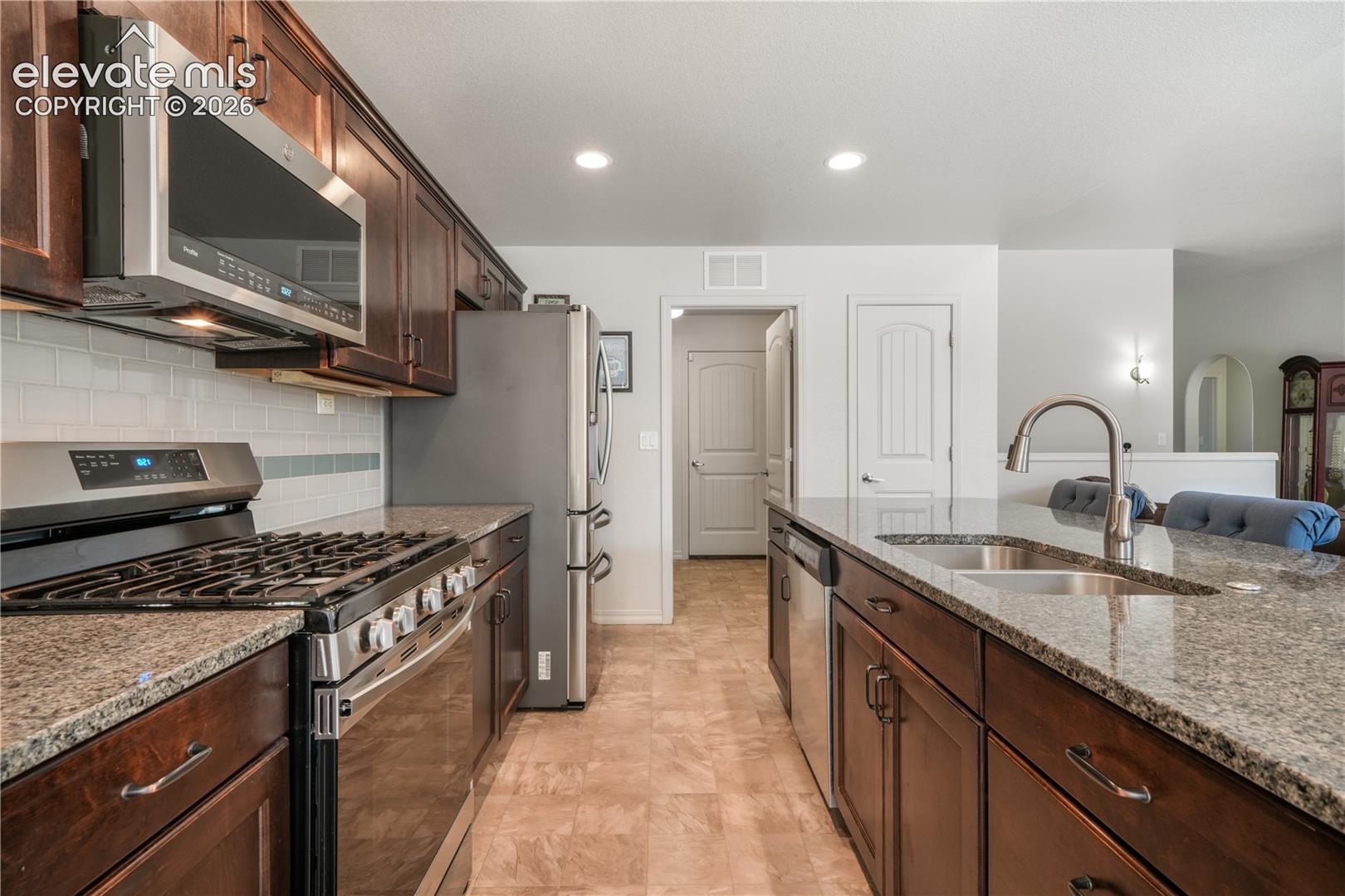 Kitchen with large island, granite countertops, gas range, abundant cabinets, views into laundry room and then access to the garage