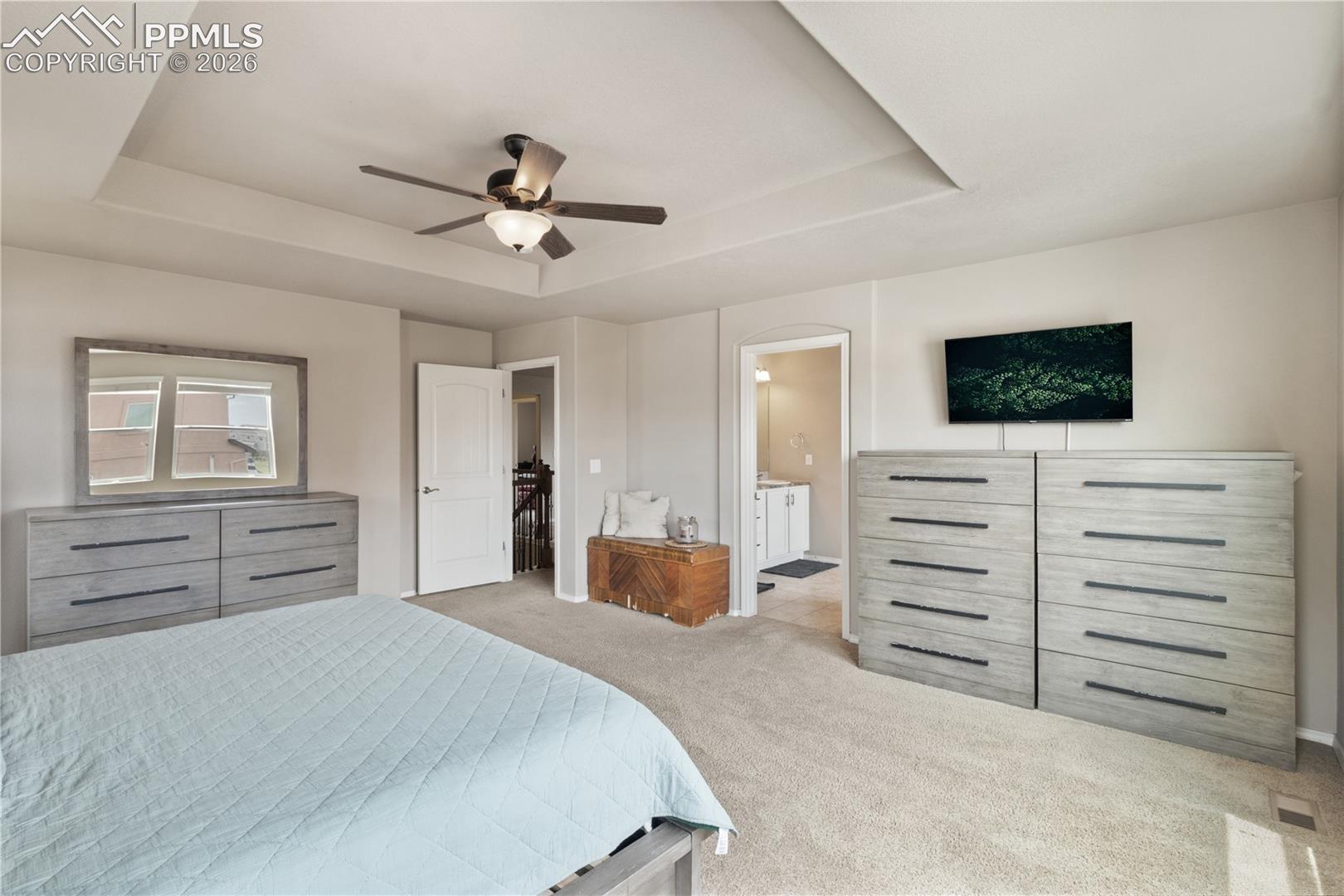 Bedroom featuring light colored carpet, a raised ceiling, ceiling fan, and ensuite bathroom