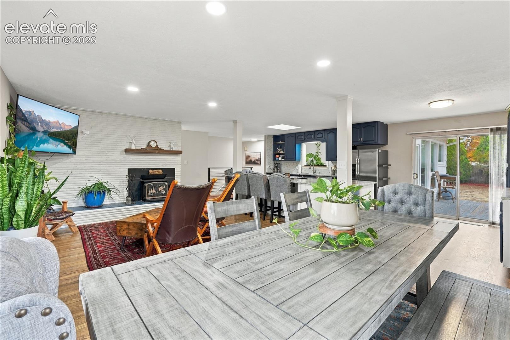 Open-concept area featuring white-painted brick fireplace with wood mantel, wood-finish flooring, recessed lighting, navy cabinetry, and sliding glass doors to the exterior