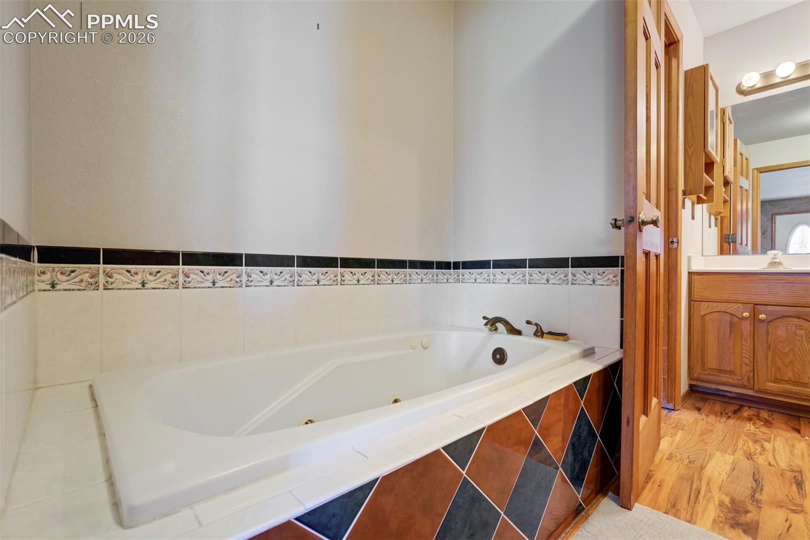 Built-in soaking tub with brass fixtures, surrounded by white tile with a decorative border
