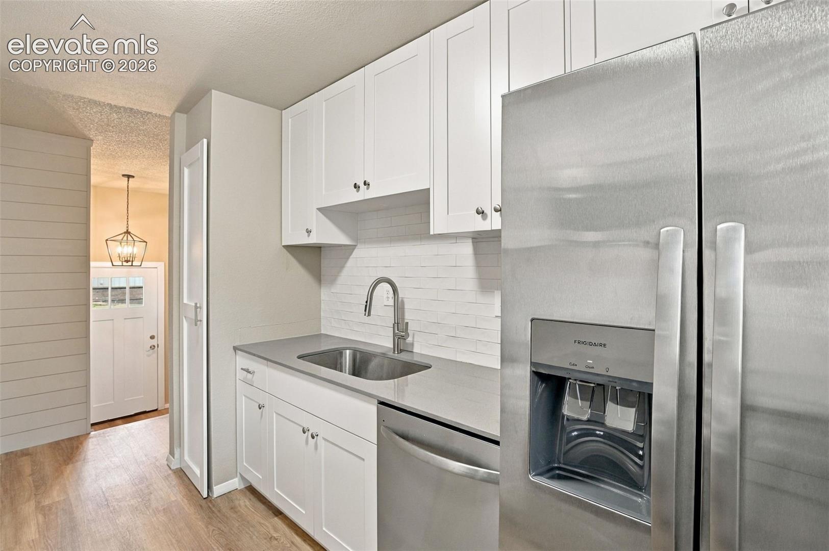 Kitchen featuring white shaker-style cabinetry, stainless steel appliances, neutral stone-surface countertops, white subway tile backsplash, and wood-finish flooring