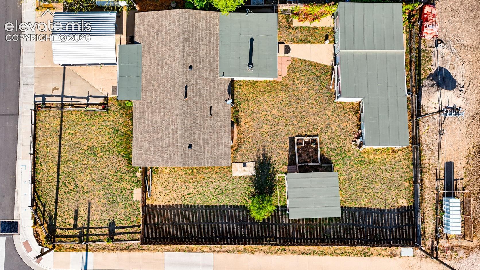 Birds eye view aerial view highlighting the property's layout, fenced yard, covered carport, detached workshop and storage buildings, screened enclosure, and outdoor garden areas.