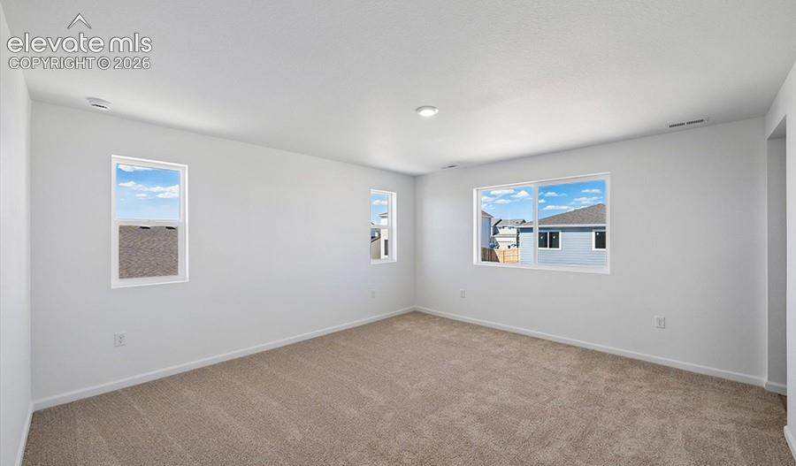 Spacious interior room featuring neutral wall paint, carpeted flooring, and multiple sliding and single-hung windows
