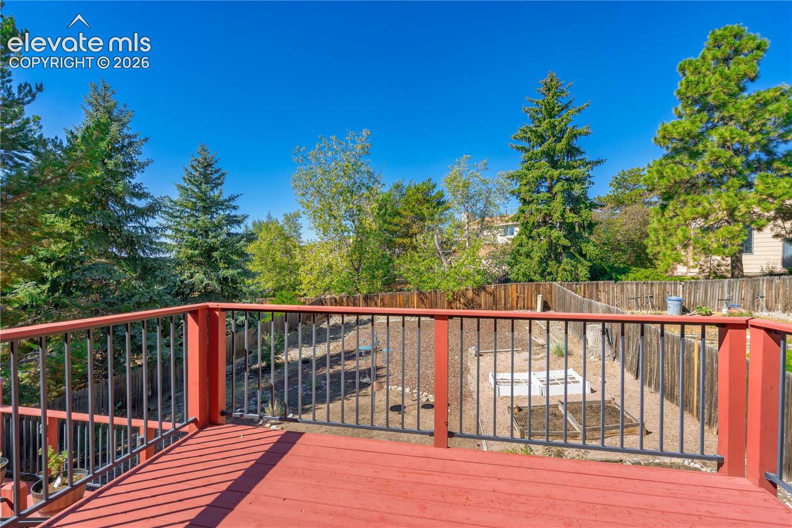 Expansive deck with red wood flooring and black metal railings, overlooking a terraced yard with mature trees and wood fencing