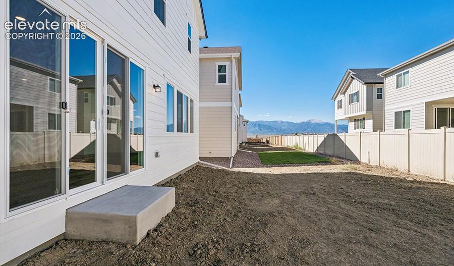Exterior featuring white horizontal siding, large sliding glass doors, concrete step, and perimeter fencing with mountain scenery