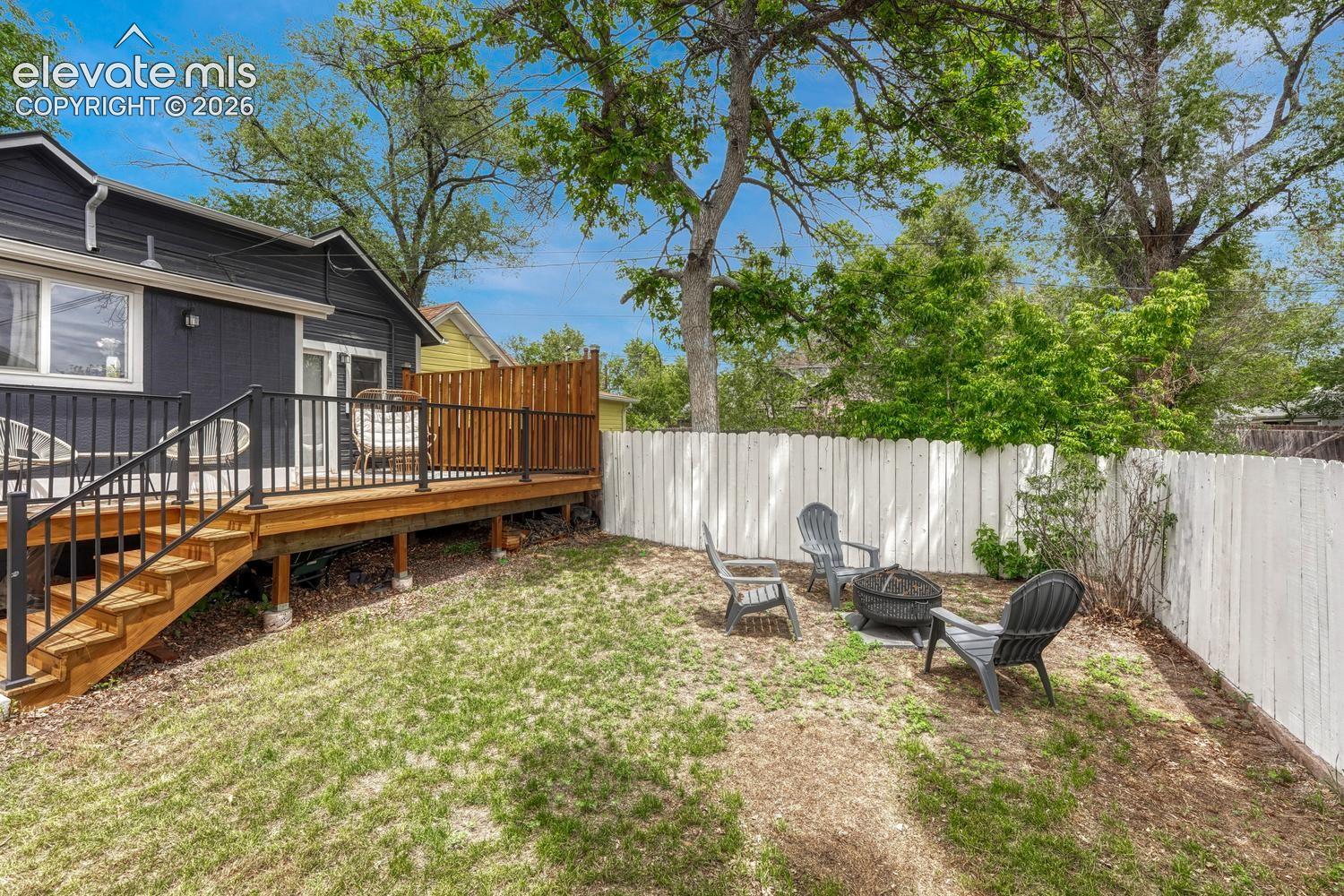Private backyard featuring a wood deck with black metal railings, a white picket fence, and a sloped lawn