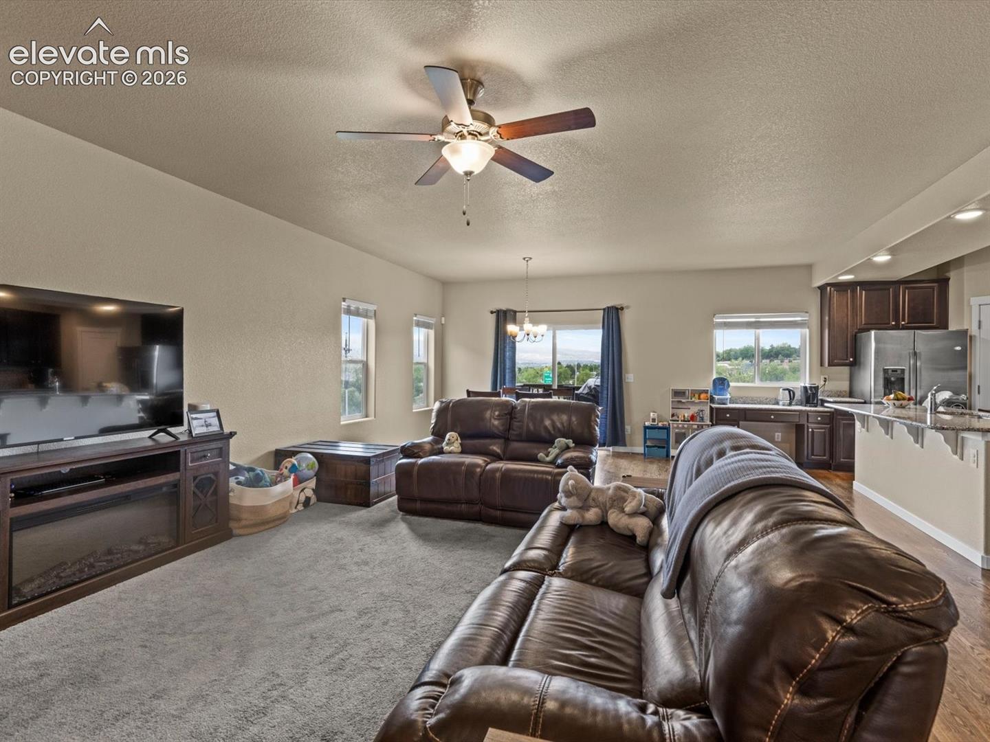 Open-concept living space featuring carpeted flooring, a ceiling fan, and multiple windows