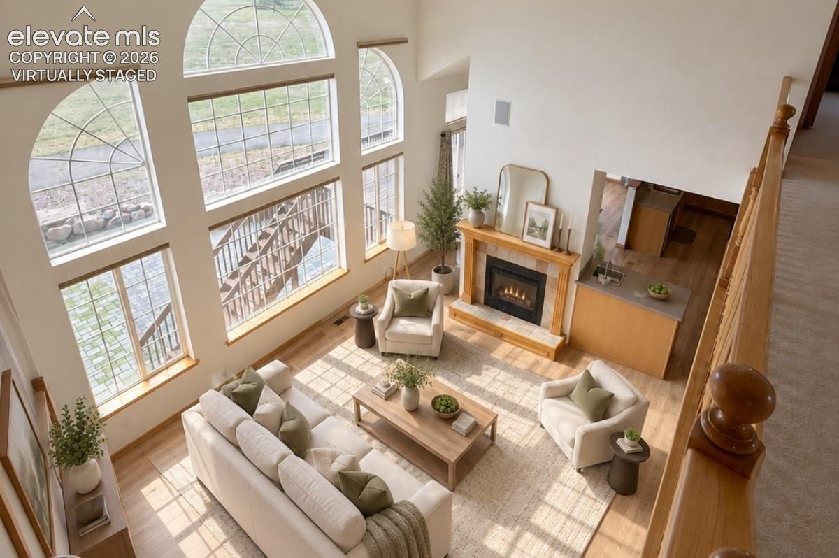 Two-story living area with expansive arched windows, a gas fireplace with a wood mantel, wood-finish flooring, and a built-in wet bar with a sink. Virtually staged