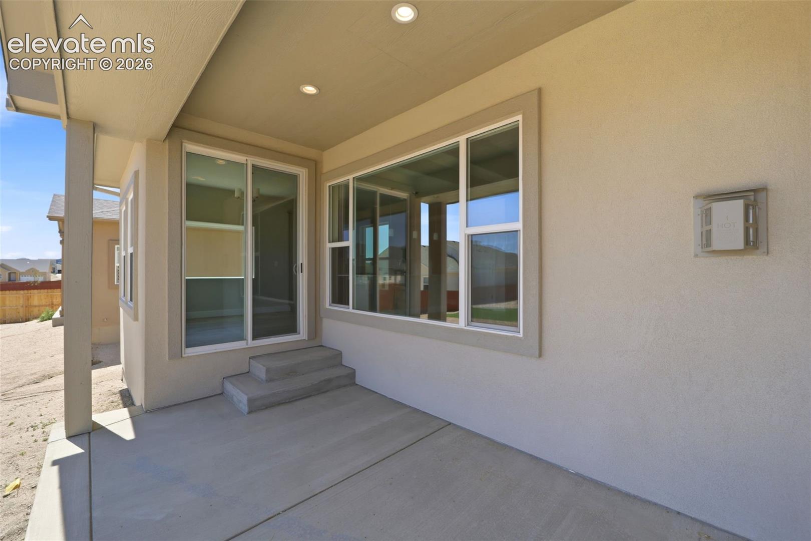Covered concrete patio featuring recessed lighting, large pane windows, and a sliding glass door with concrete step entry
