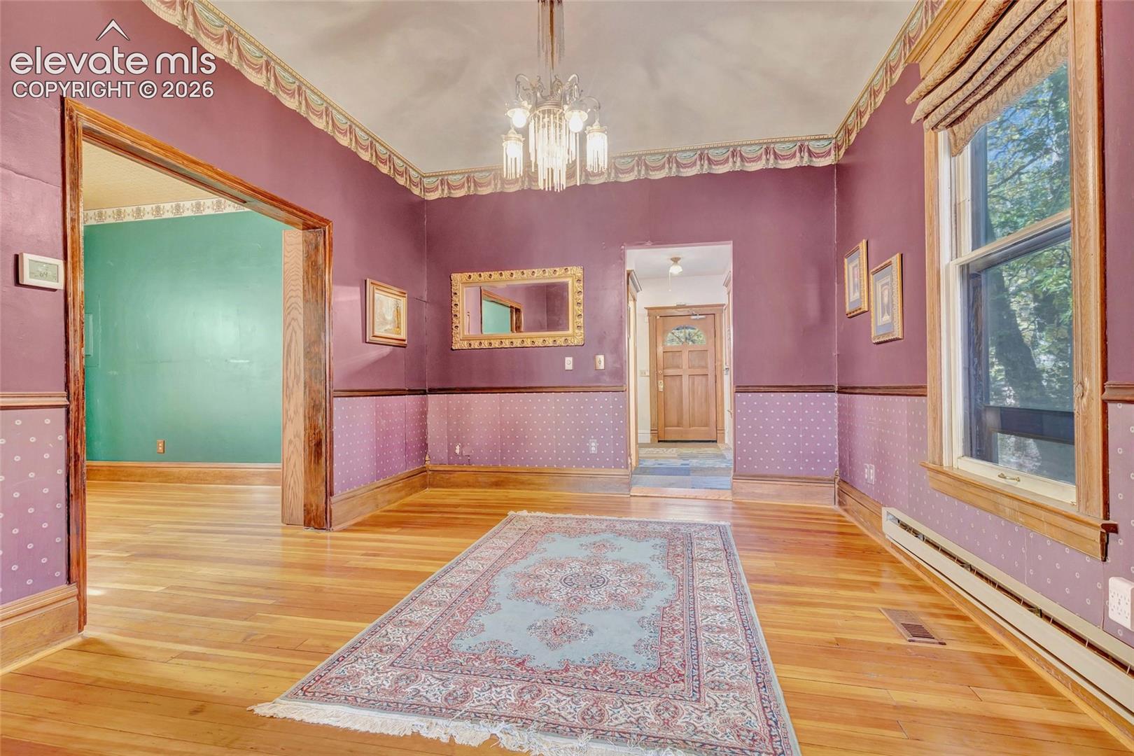 Hardwood flooring, crown molding with decorative border, multi-pane window with wood trim, built-in wall mirror, and tiered glass chandelier