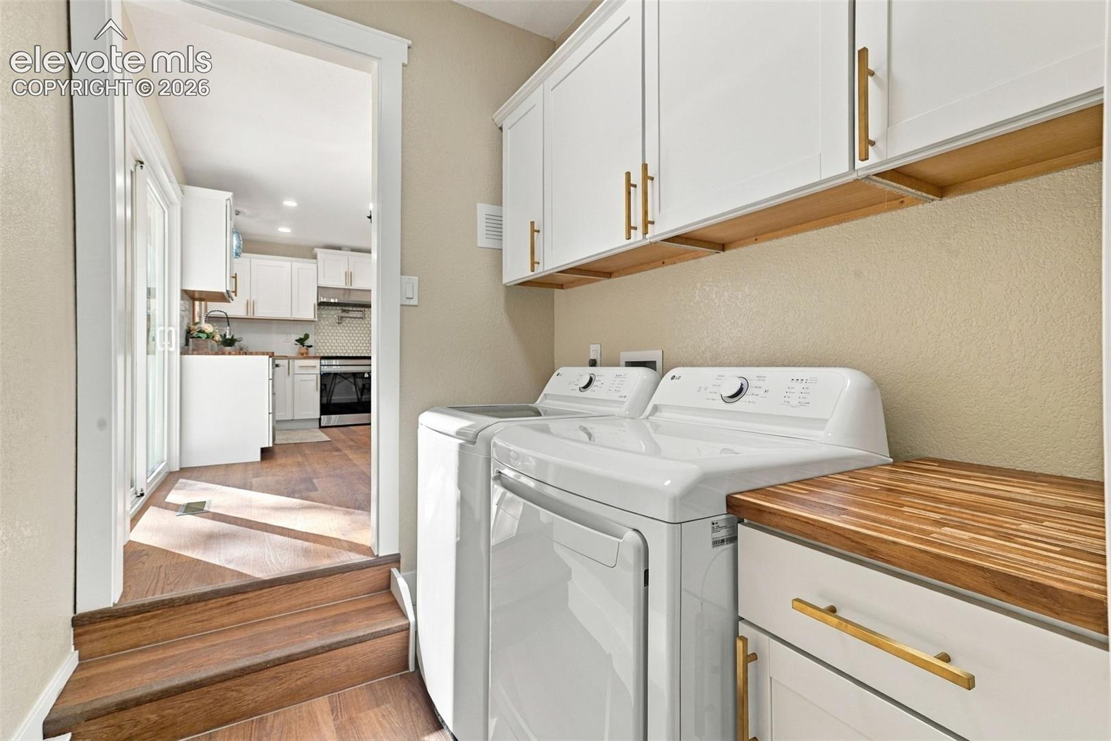 Laundry room featuring white cabinetry, butcher block-style countertops, matte gold hardware, and wood-finish flooring