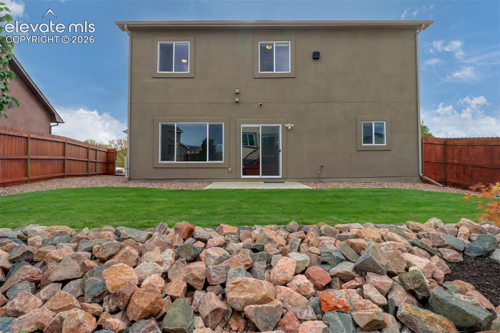 Two-story exterior featuring stucco siding, a concrete patio, a manicured lawn, and perimeter wood fencing