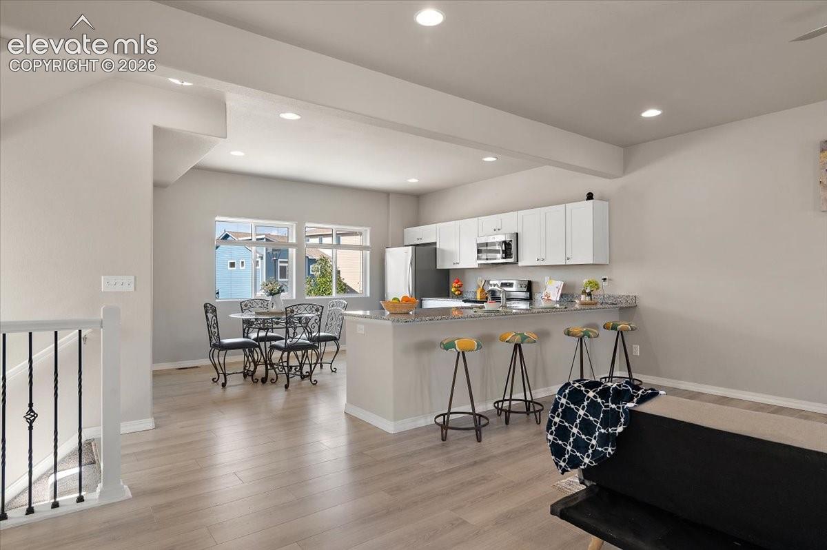 Recessed lighting, wood-finish flooring, white cabinetry, stainless steel appliances, and a kitchen island with stone countertop