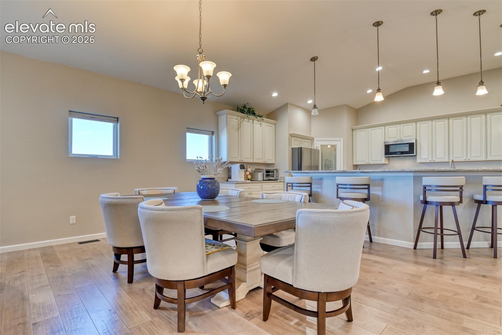Open-concept living space with wood-finish flooring, vaulted ceilings, recessed lighting, a breakfast bar, and white cabinetry.