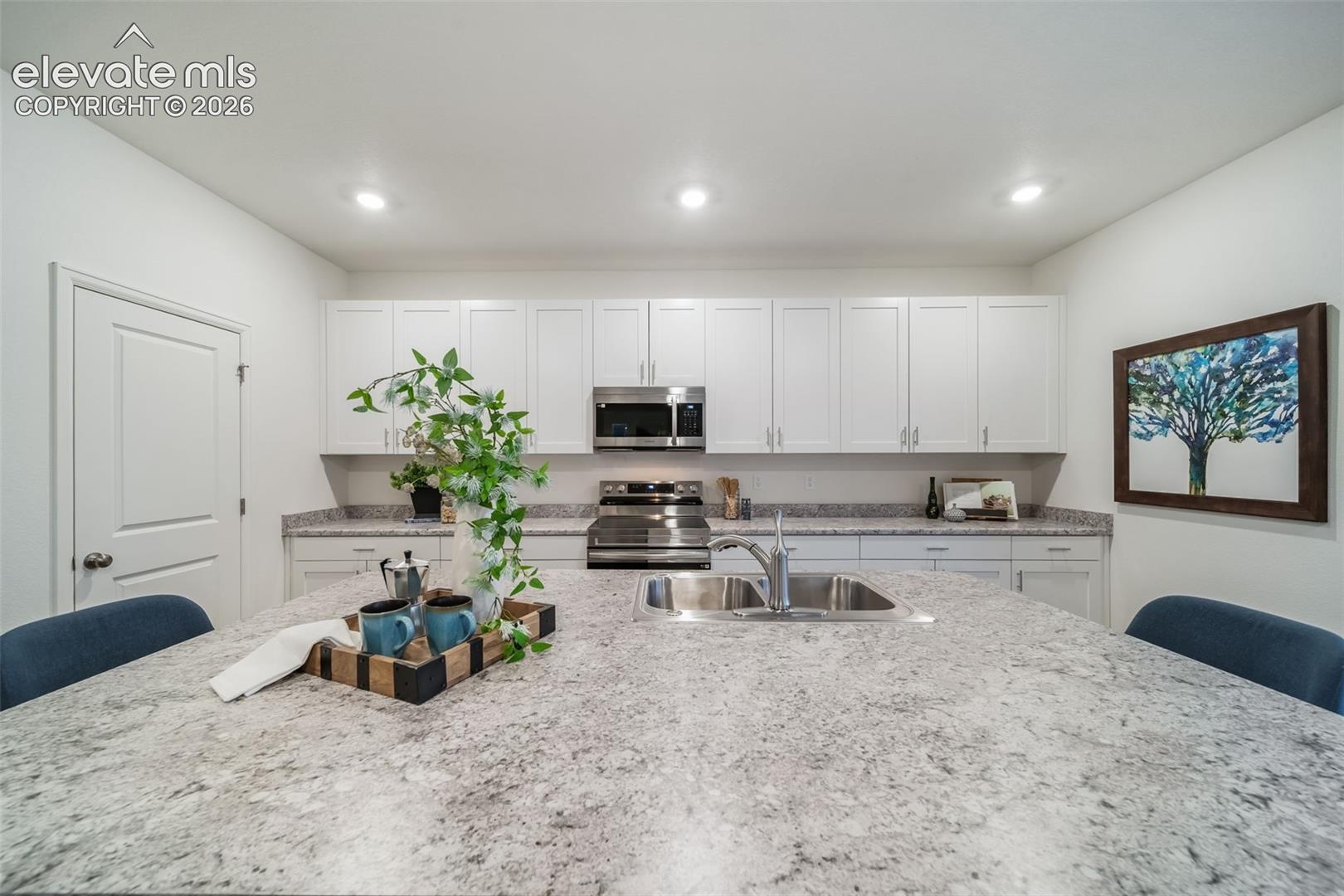 Kitchen island with an undermount sink and polished chrome faucet, white cabinetry, integrated stainless steel appliances, and recessed lighting
*photos of a model home*