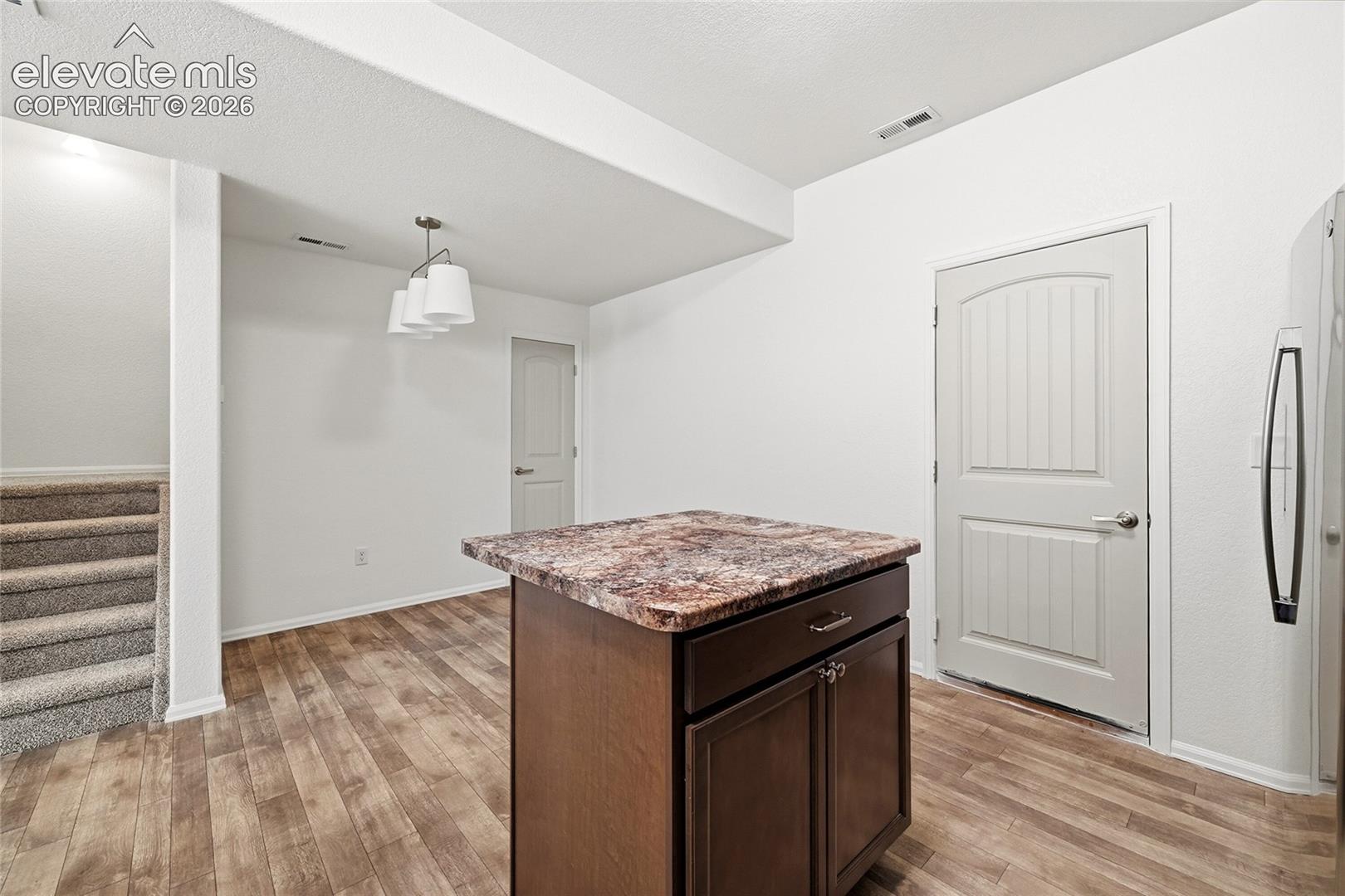 Kitchen island featuring dark wood cabinetry and a patterned countertop, wood-finish flooring, and a multi-light pendant fixture