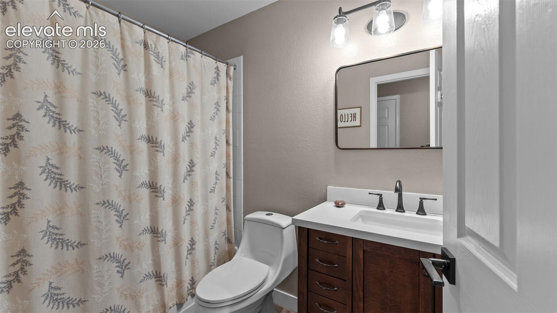 Bathroom featuring a vanity with wood-finish cabinetry, a white countertop, an integrated rectangular sink, matte black widespread faucet, and a wall-mounted mirror