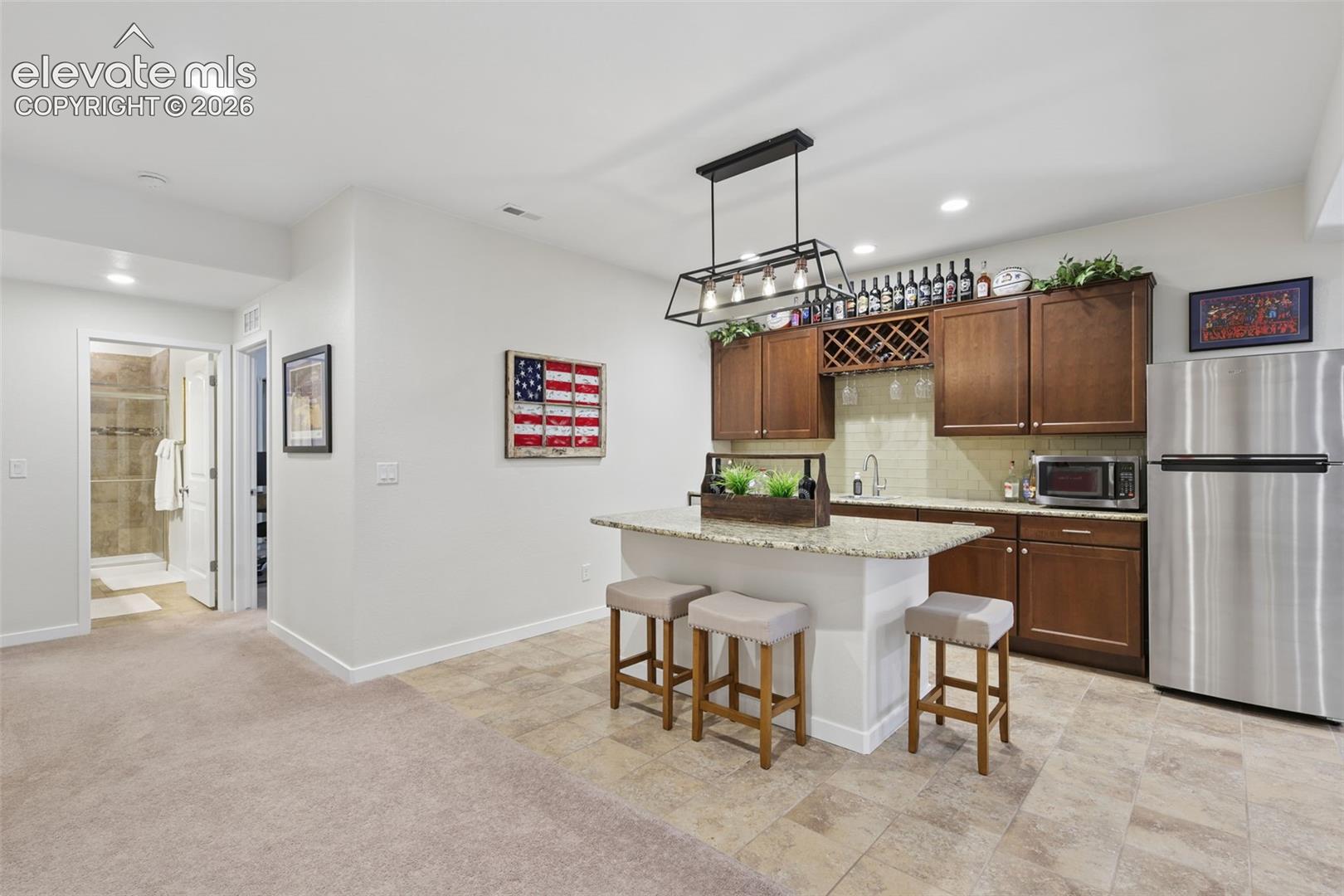 Built-in wet bar with wood cabinetry, granite-style countertop, and tile flooring