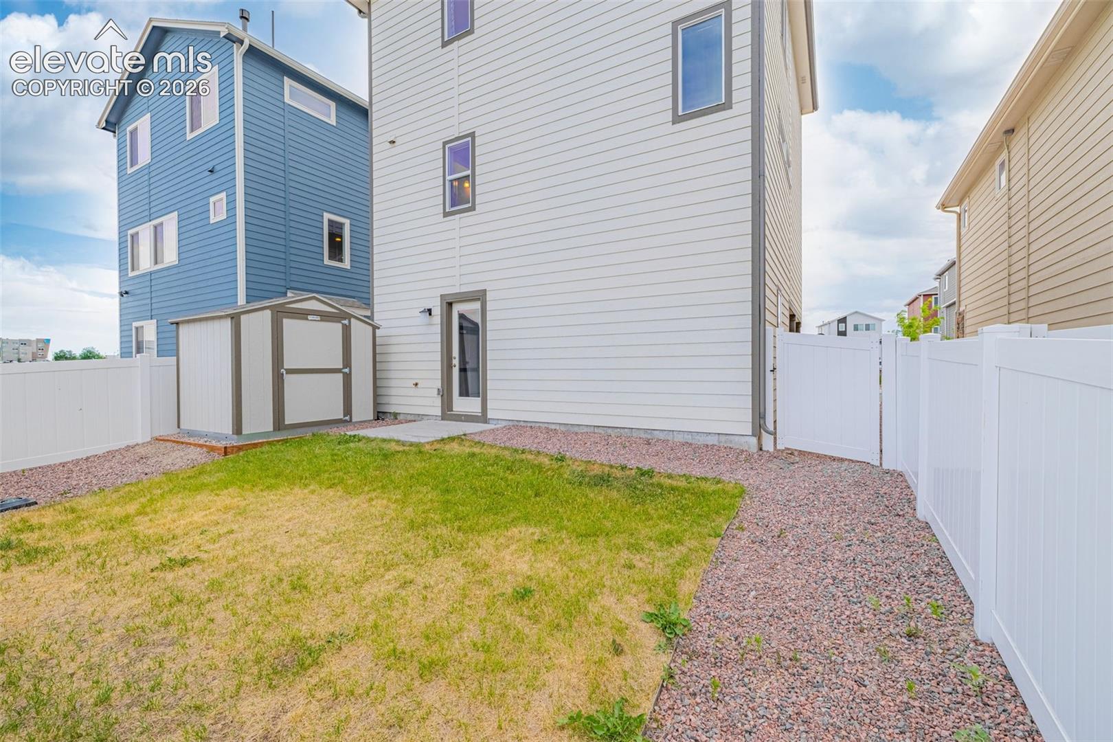 Rear exterior featuring a privacy fence, gravel pathway, and a storage shed