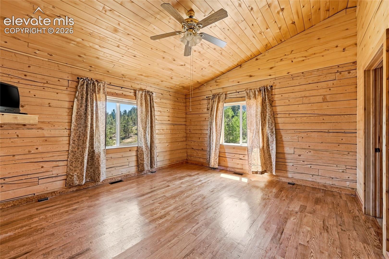 Vaulted wood-paneled ceiling, wood-plank walls, wood-finish flooring, two windows, and a ceiling fan