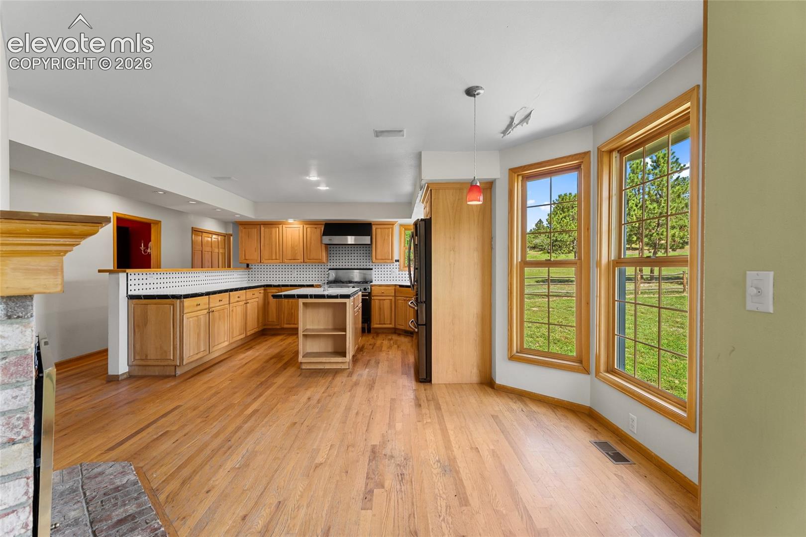 Kitchen with wood-finish flooring, light wood cabinetry, and a black and white tiled backsplash