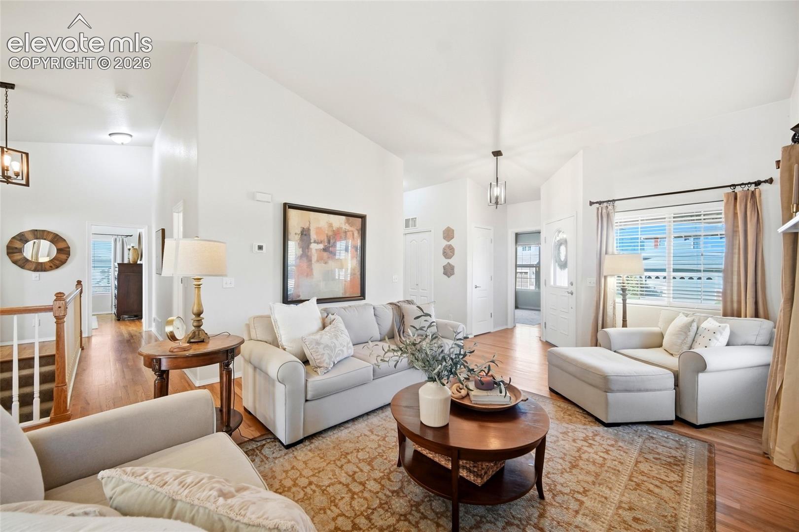 Vaulted ceiling, hardwood flooring, white interior walls, white trim, and a prominent window