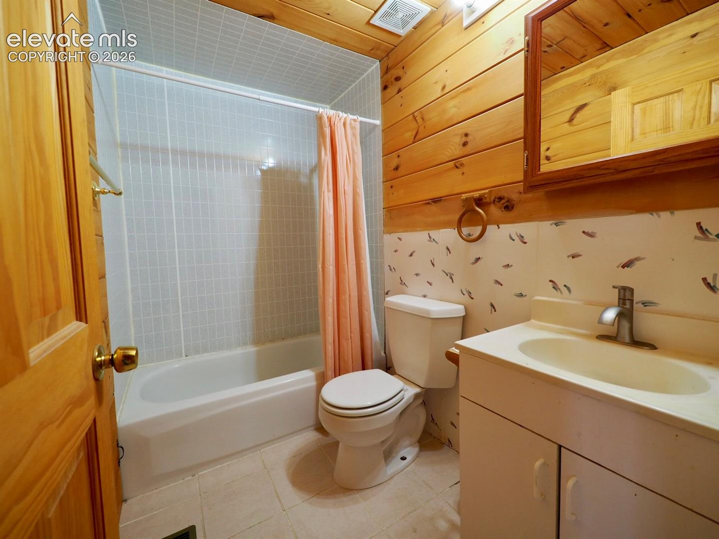 Bathroom featuring horizontal wood-plank wall paneling, a combination tub and shower with white tile surround, a built-in vanity cabinet with an integrated sink, and a framed wall-mounted mirror