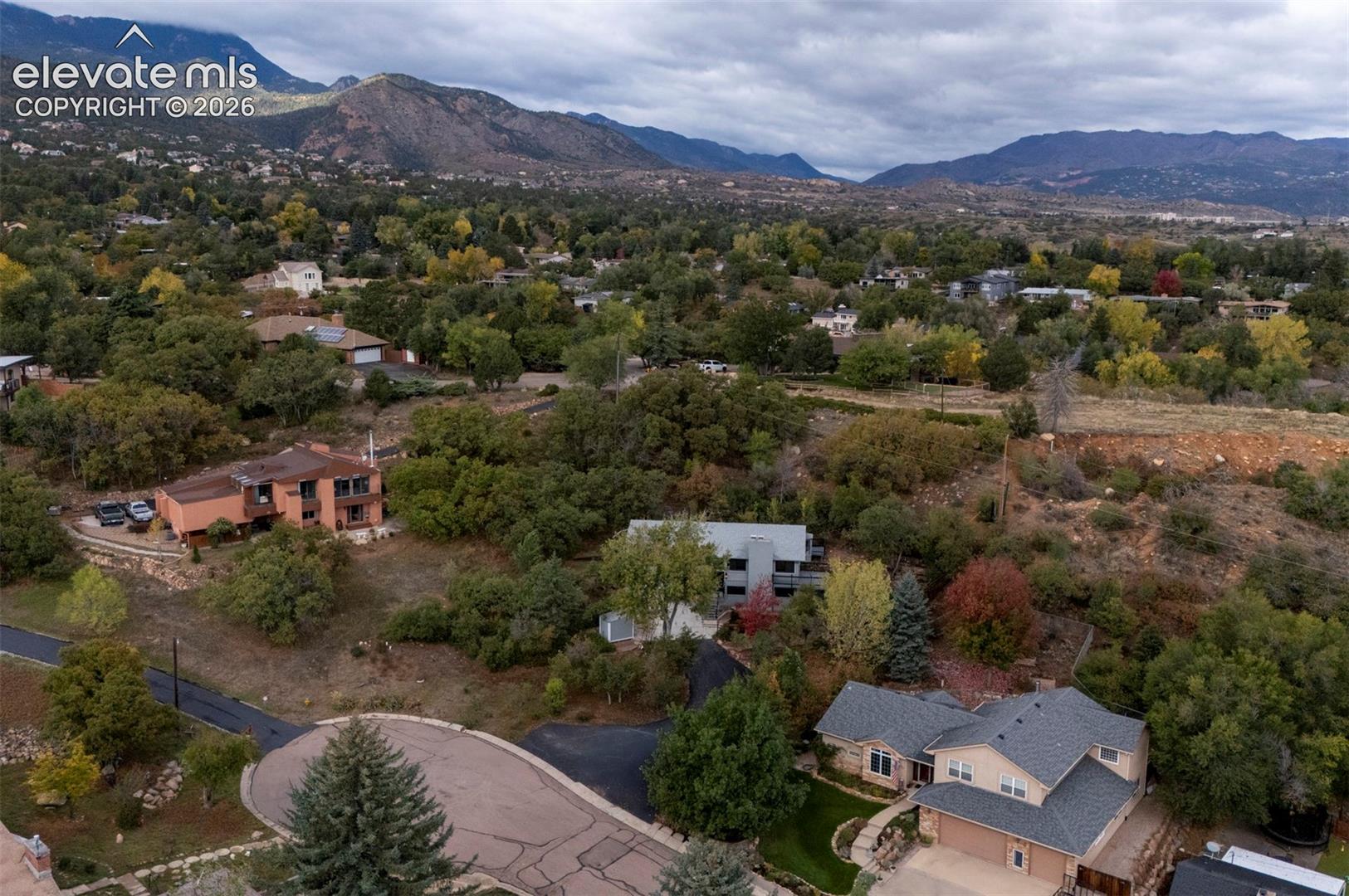 Aerial perspective featuring multi-story residential structures, mature deciduous and evergreen trees, paved cul-de-sac infrastructure, and a prominent mountain range backdrop