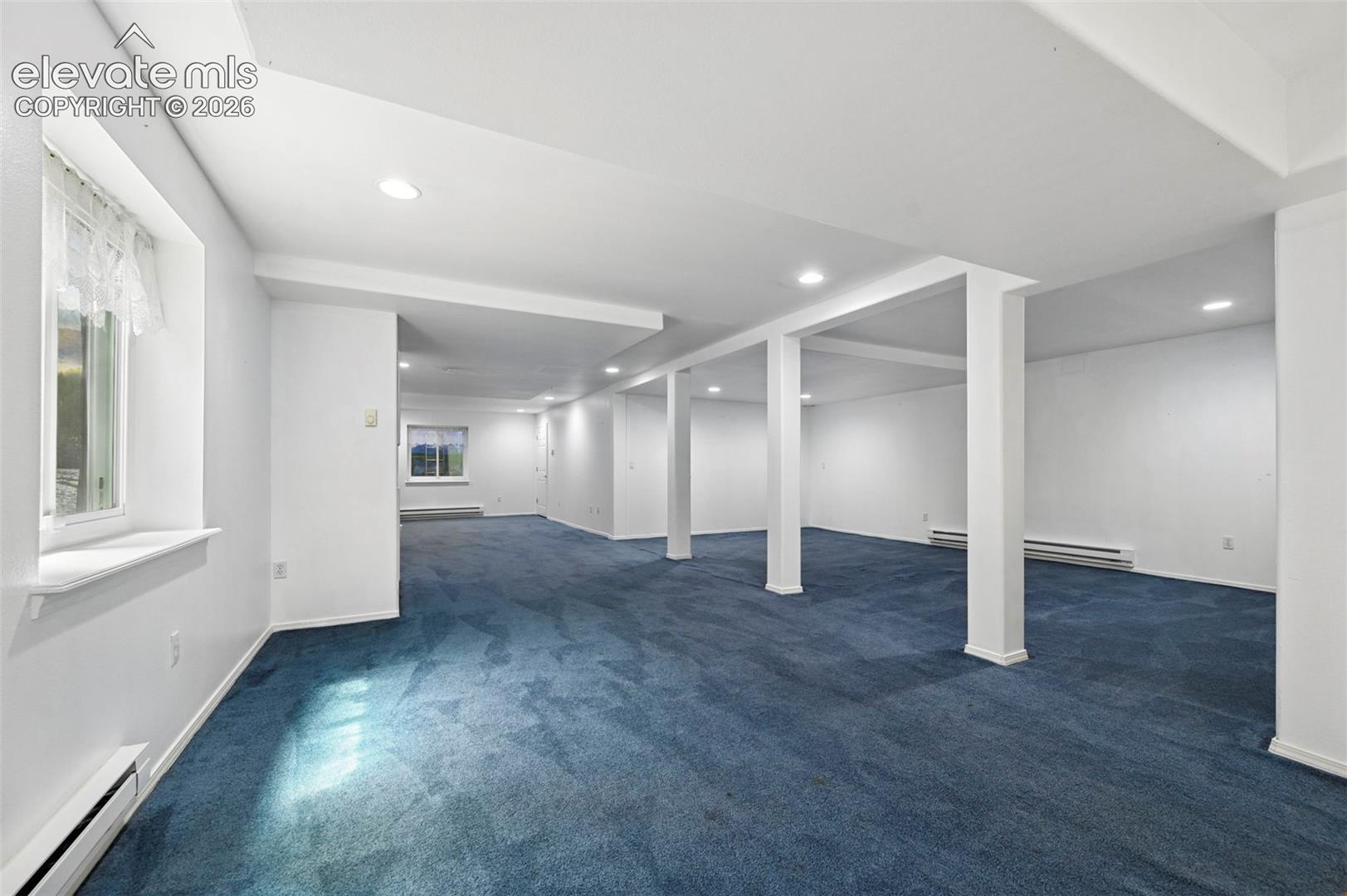 Expansive room with recessed lighting, multiple windows, carpet flooring, and support columns