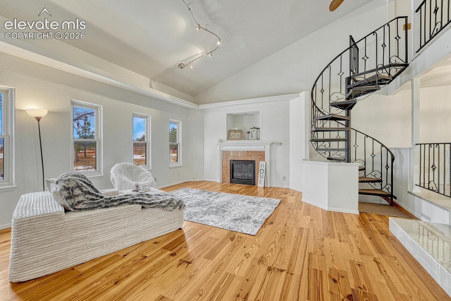 Cozy living room with vaulted ceilings and natural wood floors. View of custom spiral staircase to loft.
