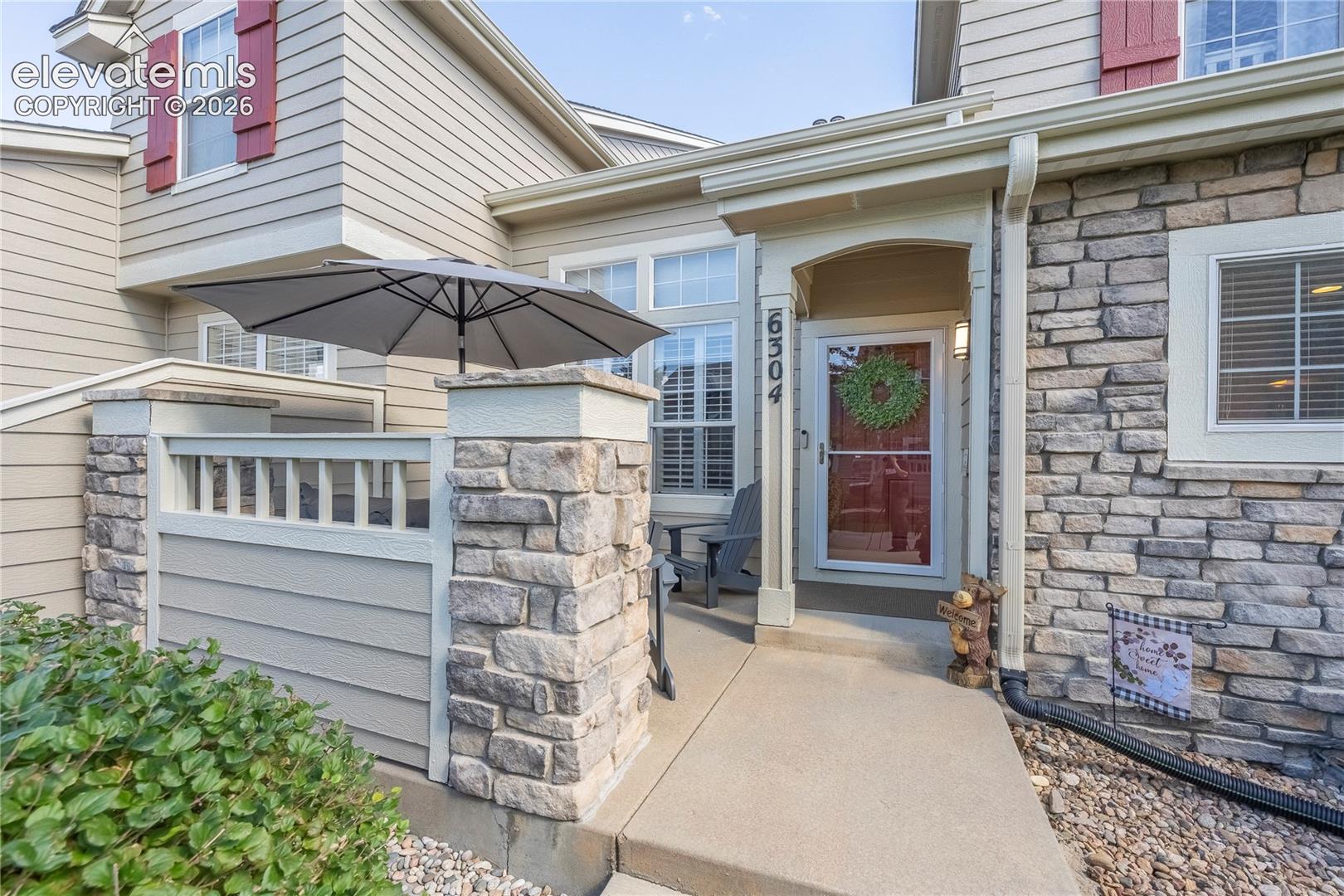 Exterior facade featuring horizontal lap siding, stone veneer accents, decorative shutters, a concrete entryway, and a private patio enclosed by stone-capped railing