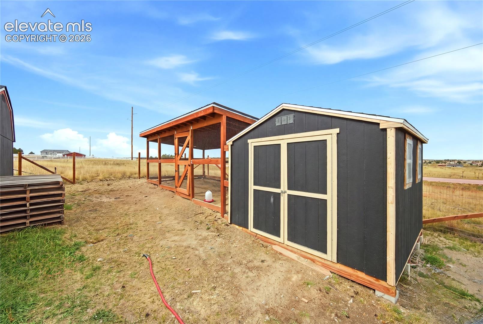 Storage shed featuring dark-toned siding with light-colored trim and a wooden open-air lean-to structure