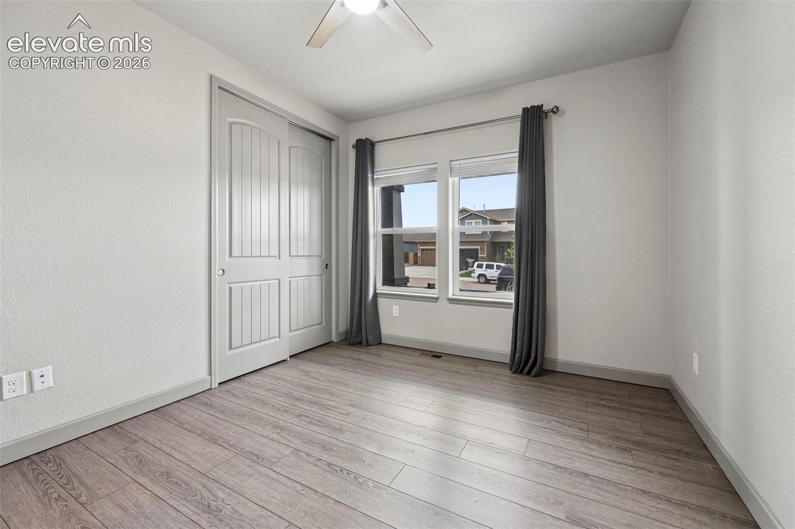 Room featuring wood-finish flooring, dual-pane windows, and a sliding closet door with a multi-panel design, completed by a ceiling-mounted light fixture