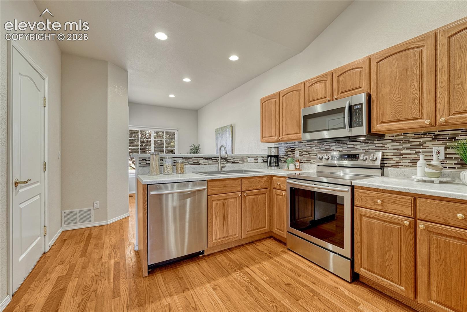 The fully equipped kitchen showcases solid oak cabinetry, beautiful tile backsplash, continuous hardwood flooring, and high-top breakfast bar
