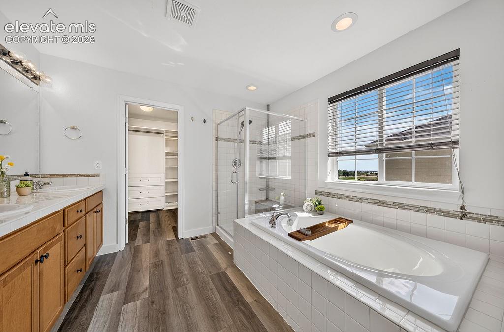 Bathroom featuring a double vanity with wood cabinetry, a glass-enclosed shower, a built-in soaking tub, and wood-finish flooring