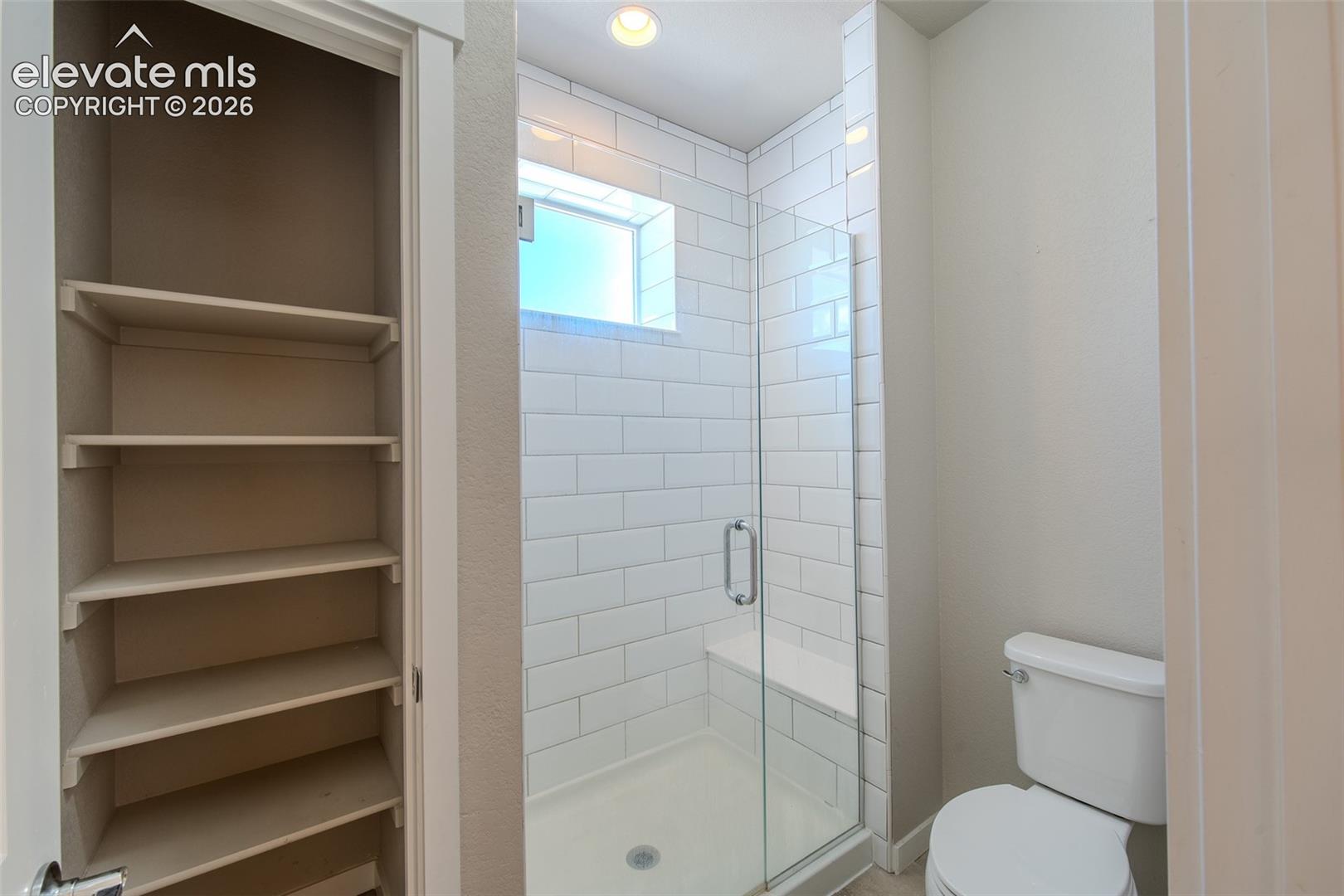 Primary Bathroom with linen closet and enclosed, tiled shower with built-in seat.