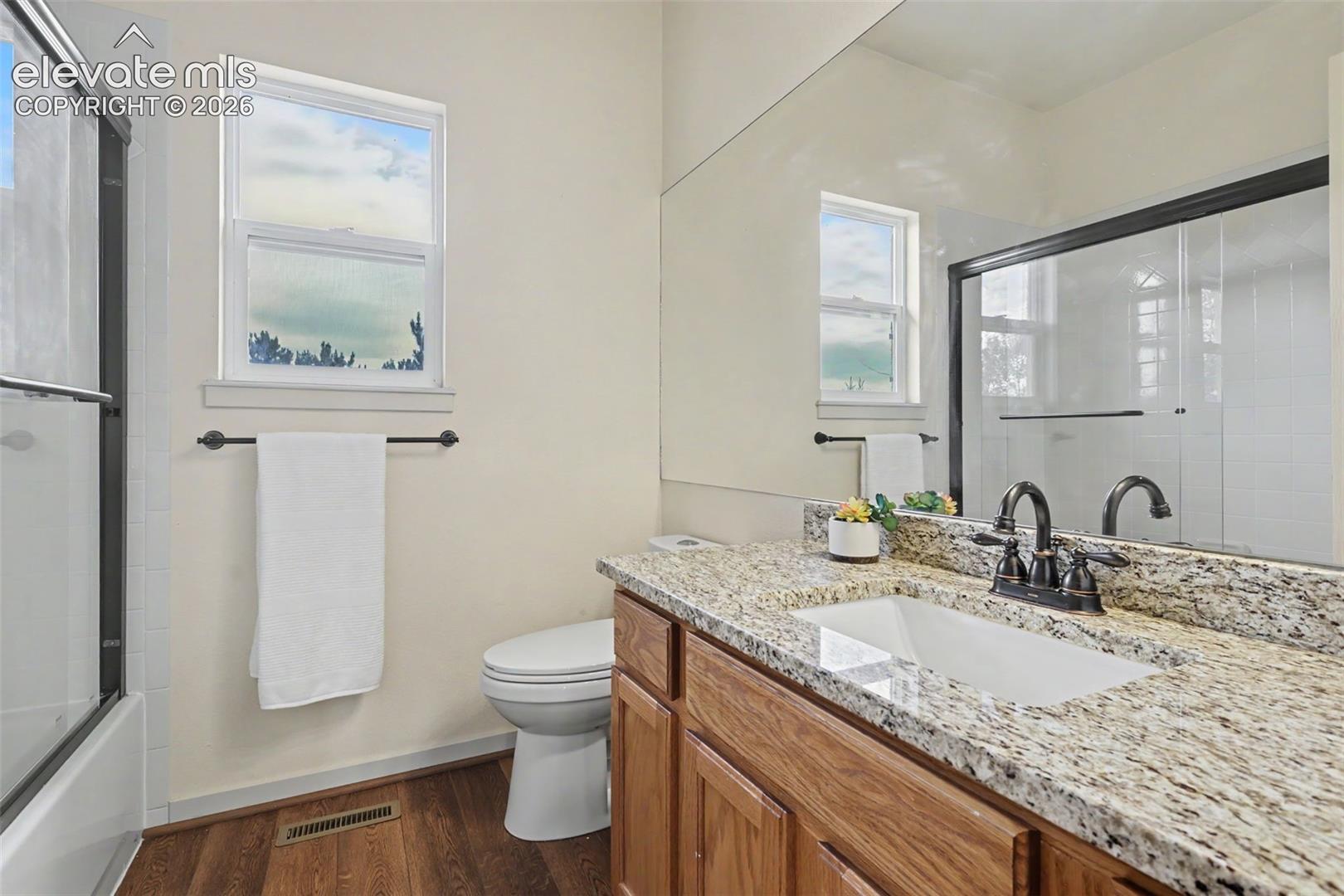 Bathroom featuring a granite-look countertop with an undermount sink, wood-finish vanity, and bronze-finish faucet